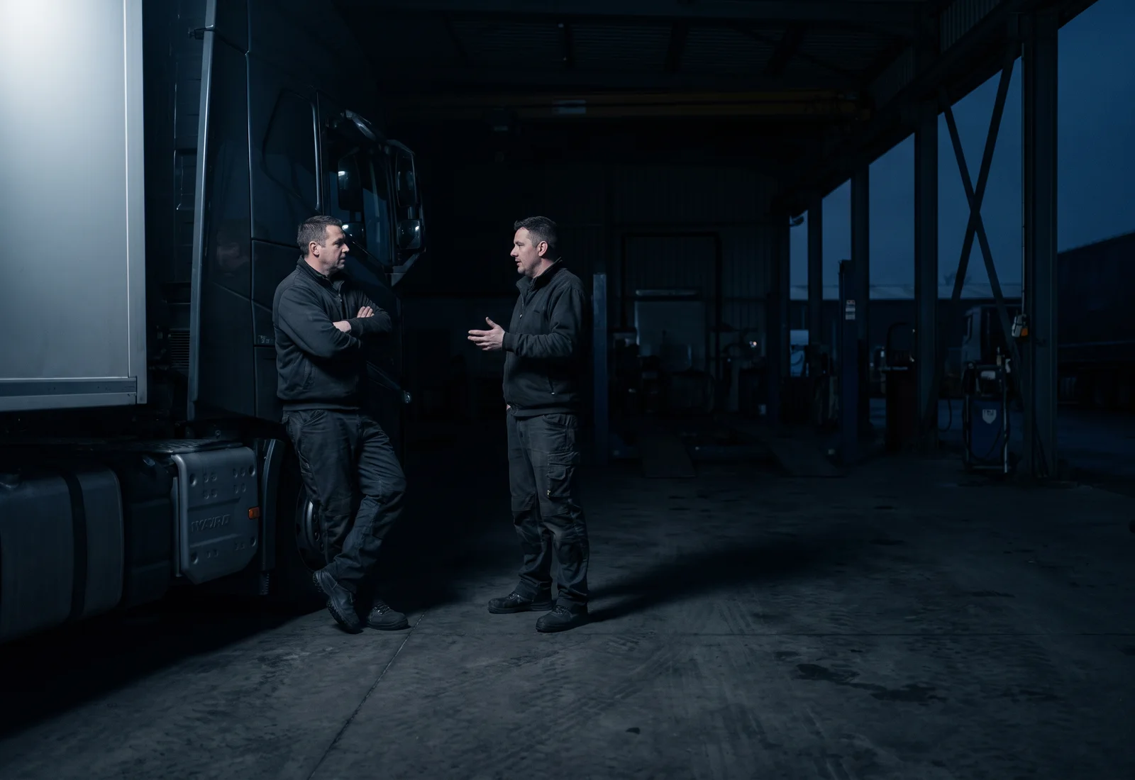 Two professional drivers talking beside a tractor unit in a maintenance bay
